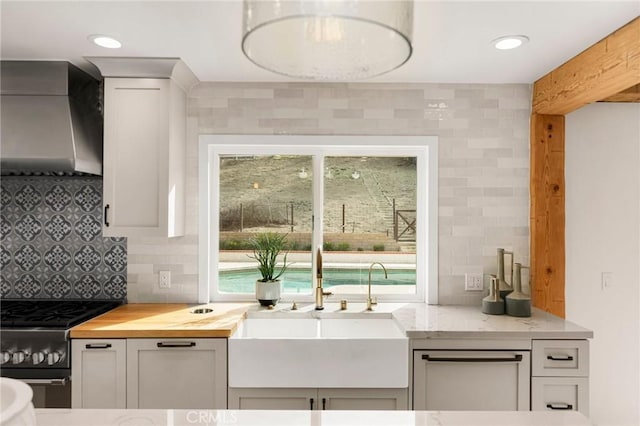 kitchen featuring white cabinetry, butcher block counters, stainless steel gas stove, and wall chimney range hood