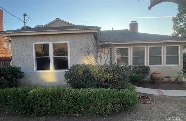 view of side of property with a chimney, a shingled roof, stucco siding, and crawl space