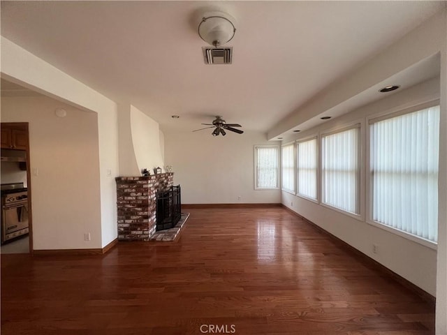 unfurnished living room with wood finished floors, ceiling fan, a brick fireplace, baseboards, and visible vents