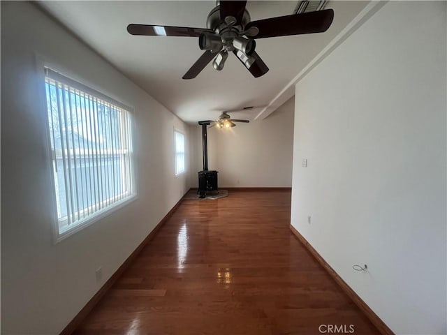 interior space with a wood stove, a ceiling fan, wood finished floors, and baseboards