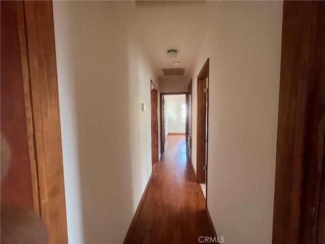 corridor with baseboards, visible vents, and wood finished floors