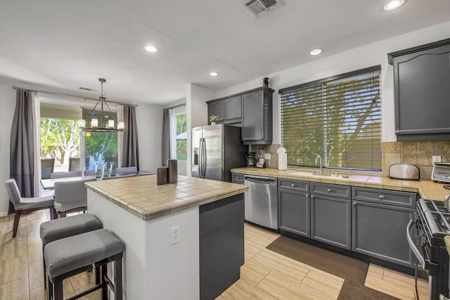 kitchen with tile counters, decorative light fixtures, appliances with stainless steel finishes, and sink