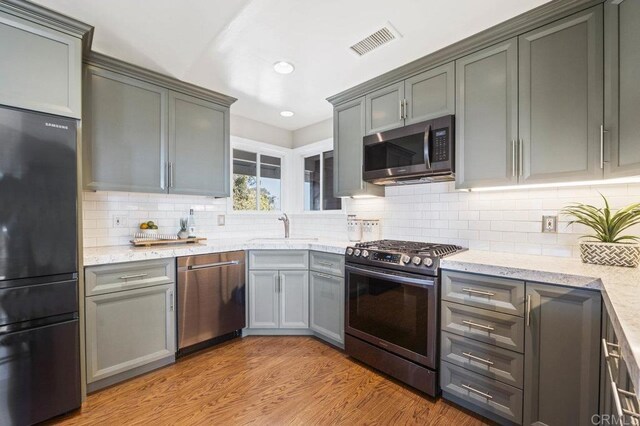 kitchen with tasteful backsplash, sink, light wood-type flooring, stainless steel appliances, and light stone counters