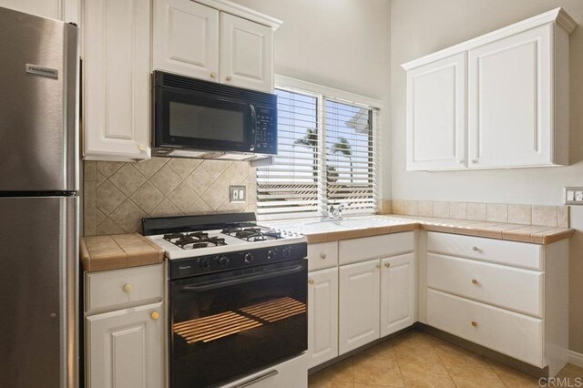 kitchen with tasteful backsplash, tile countertops, stainless steel refrigerator, white range with gas stovetop, and white cabinets