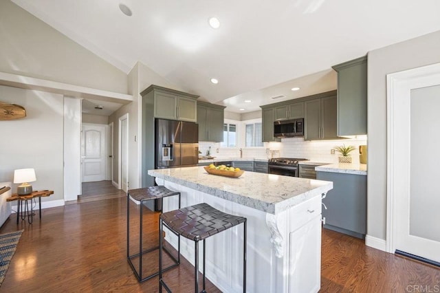 kitchen featuring appliances with stainless steel finishes, decorative backsplash, vaulted ceiling, a kitchen island, and light stone counters