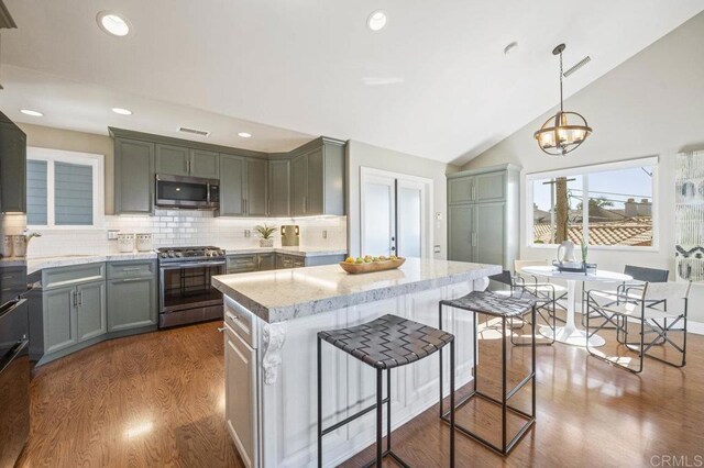 kitchen with decorative light fixtures, vaulted ceiling, a kitchen island, decorative backsplash, and appliances with stainless steel finishes