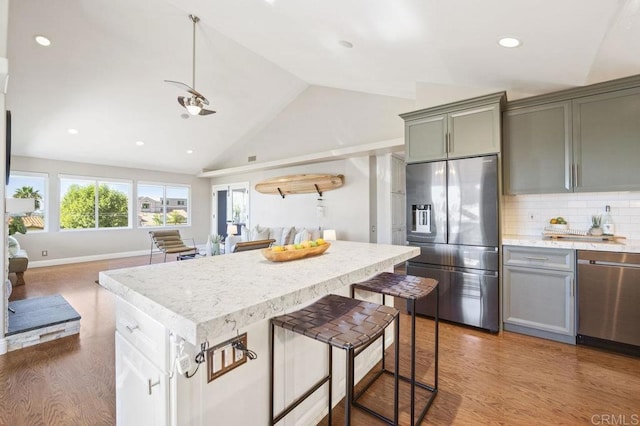 kitchen featuring hardwood / wood-style floors, stainless steel appliances, decorative backsplash, high vaulted ceiling, and a kitchen island