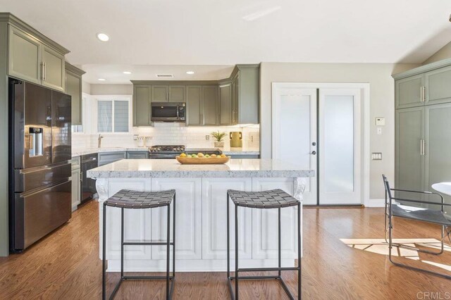 kitchen with appliances with stainless steel finishes, green cabinets, a breakfast bar area, and light hardwood / wood-style flooring