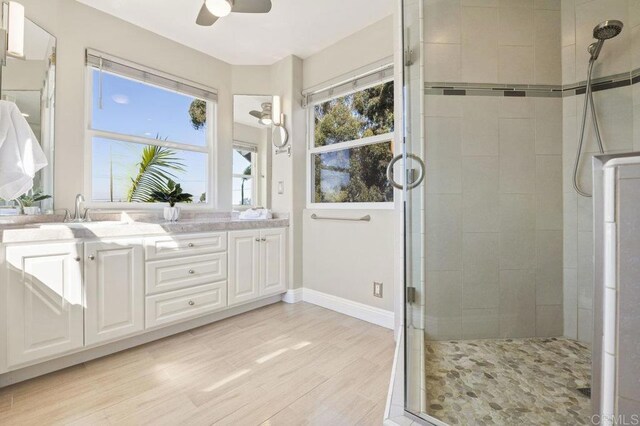 bathroom with ceiling fan, hardwood / wood-style floors, a shower with shower door, and vanity