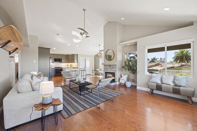 living room featuring ceiling fan, hardwood / wood-style floors, high vaulted ceiling, and a fireplace