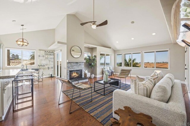 living room with ceiling fan with notable chandelier, plenty of natural light, dark hardwood / wood-style flooring, and a stone fireplace