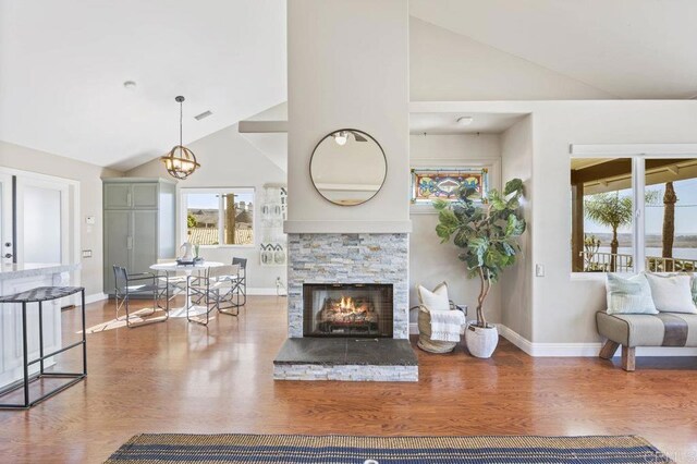 living room featuring hardwood / wood-style flooring, a notable chandelier, high vaulted ceiling, and a stone fireplace