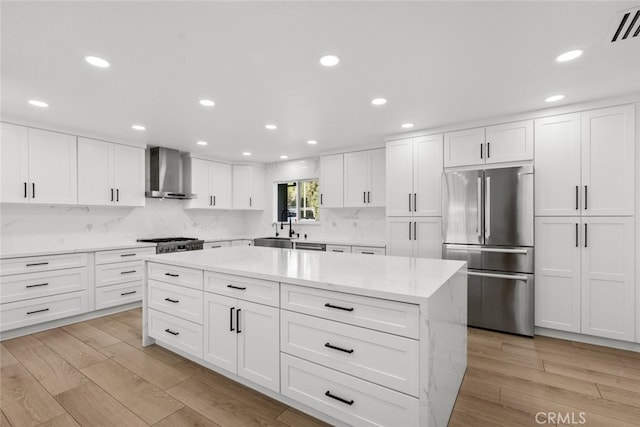 kitchen with appliances with stainless steel finishes, wall chimney exhaust hood, white cabinetry, sink, and light wood-type flooring