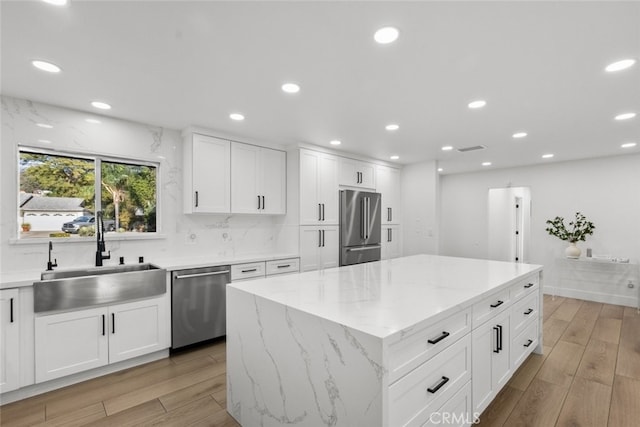 kitchen featuring a kitchen island, sink, appliances with stainless steel finishes, white cabinets, and light stone counters