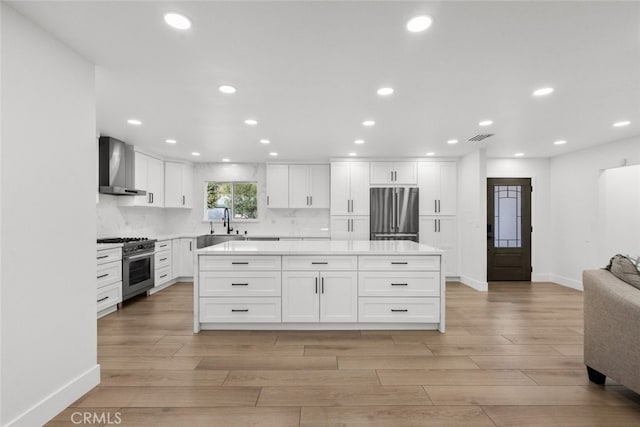 kitchen with white cabinetry, wall chimney range hood, stainless steel appliances, tasteful backsplash, and light hardwood / wood-style flooring