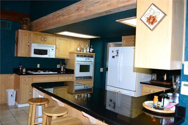 kitchen with a breakfast bar area, light tile patterned floors, light brown cabinetry, and white appliances