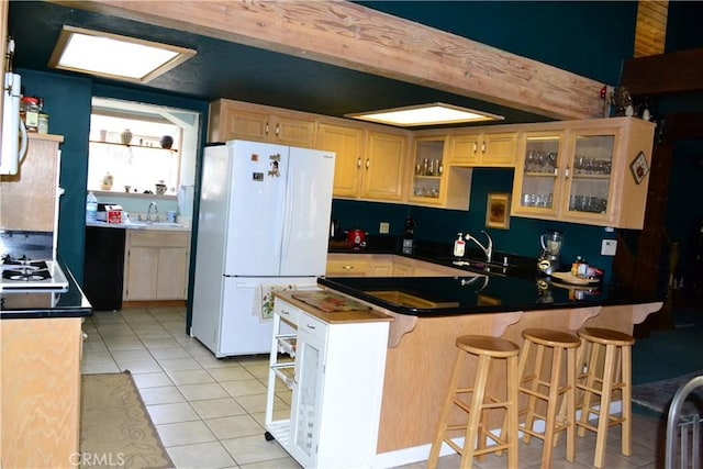 kitchen featuring white fridge, kitchen peninsula, light tile patterned flooring, a breakfast bar, and sink