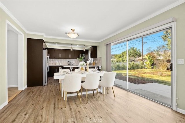 dining space with a wealth of natural light, ornamental molding, and light hardwood / wood-style flooring