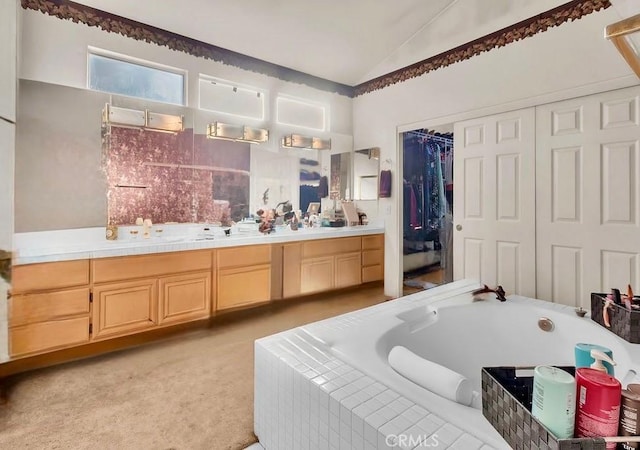 bathroom featuring tiled tub, vanity, and vaulted ceiling