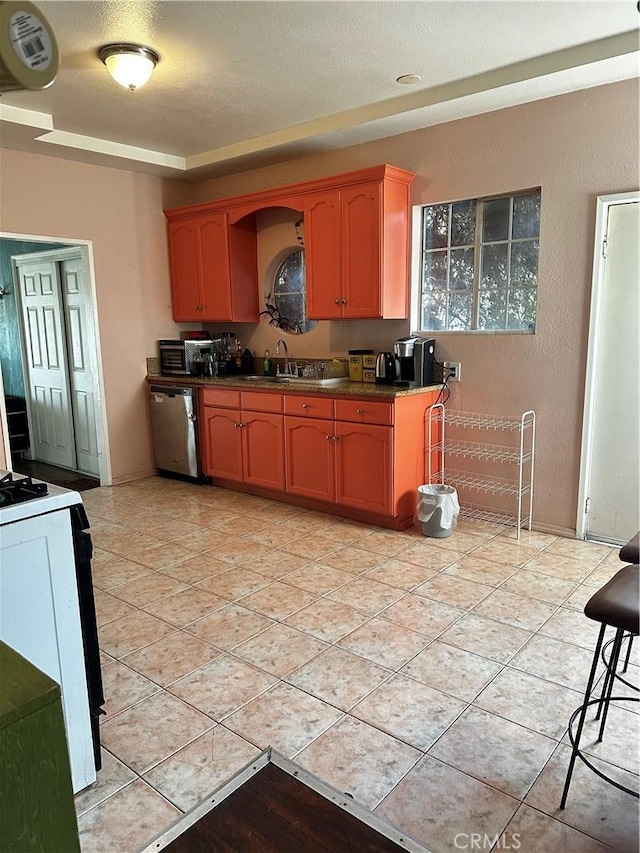 kitchen featuring stainless steel dishwasher, light tile patterned flooring, dark countertops, range with electric stovetop, and a sink
