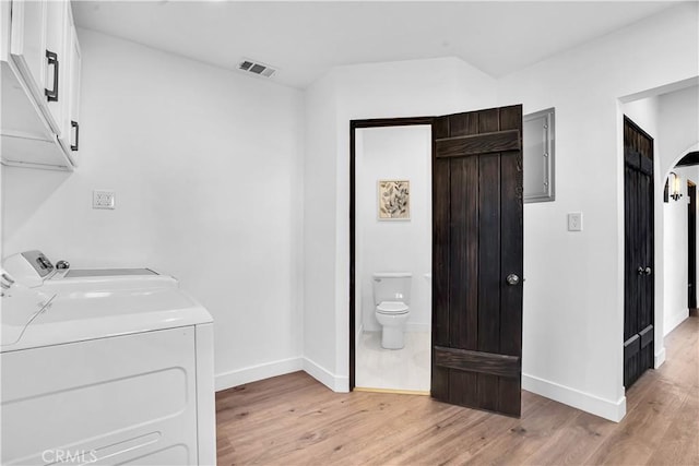 laundry room with cabinets, electric panel, washing machine and clothes dryer, and light hardwood / wood-style flooring