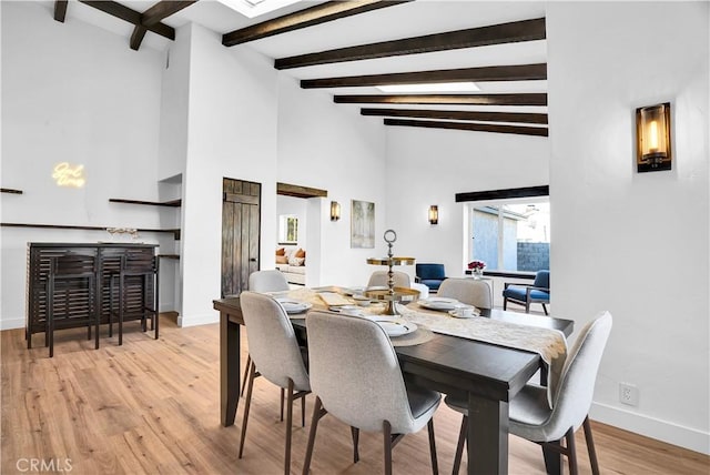 dining room featuring a towering ceiling, light hardwood / wood-style flooring, and beamed ceiling