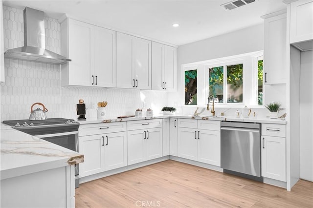 kitchen featuring white cabinetry, wall chimney range hood, appliances with stainless steel finishes, and decorative backsplash