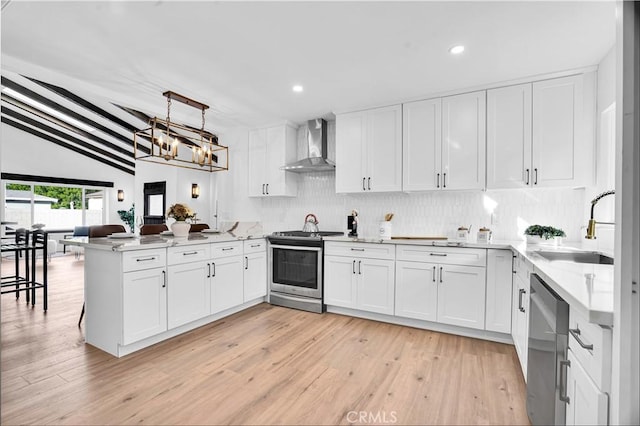 kitchen with kitchen peninsula, stainless steel appliances, tasteful backsplash, wall chimney exhaust hood, and white cabinets