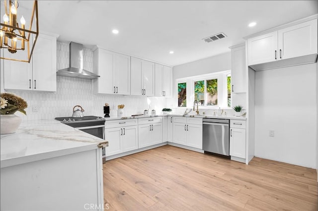 kitchen with appliances with stainless steel finishes, hanging light fixtures, light stone countertops, wall chimney exhaust hood, and white cabinets