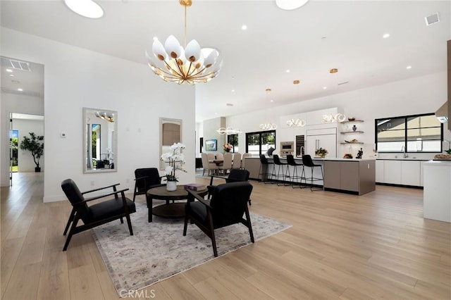 living room with a towering ceiling, a chandelier, and light hardwood / wood-style floors