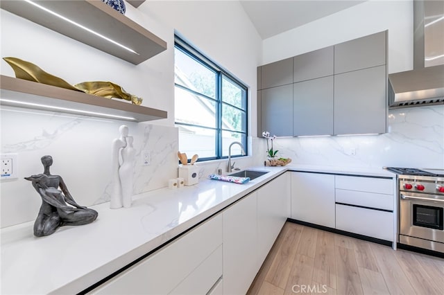 kitchen featuring luxury range, gray cabinetry, light wood-type flooring, wall chimney exhaust hood, and sink