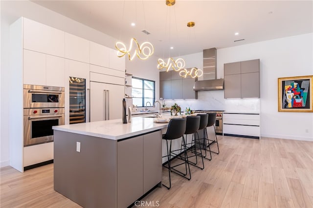 kitchen featuring decorative light fixtures, wall chimney range hood, gray cabinets, a center island with sink, and high quality appliances