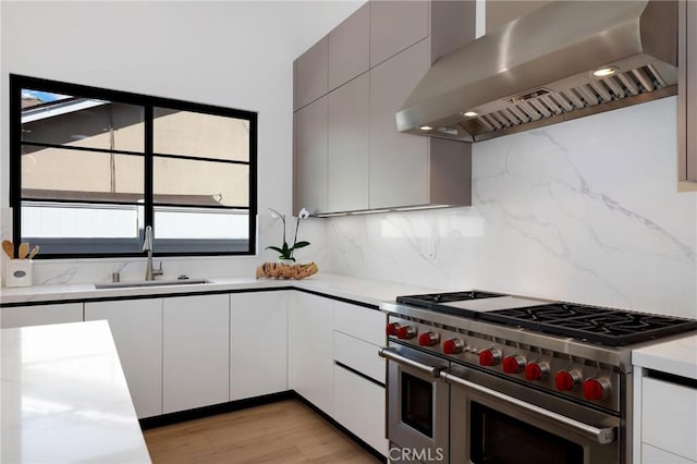 kitchen featuring backsplash, wall chimney range hood, light hardwood / wood-style floors, double oven range, and sink