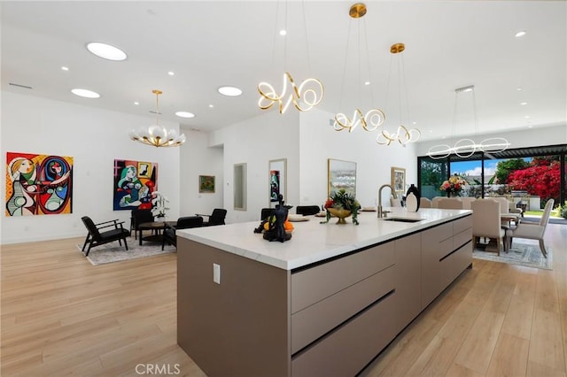 kitchen featuring an island with sink, gray cabinetry, hanging light fixtures, a chandelier, and sink