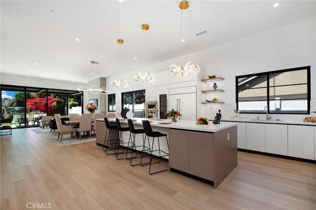 kitchen with white cabinetry, a spacious island, paneled built in refrigerator, light wood-type flooring, and pendant lighting