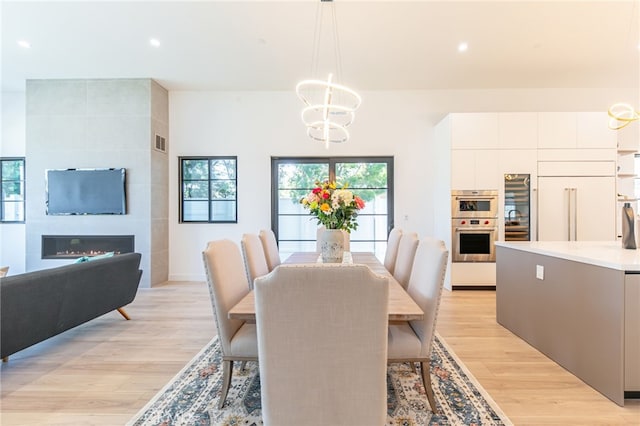 dining area with a fireplace, light hardwood / wood-style flooring, and a notable chandelier