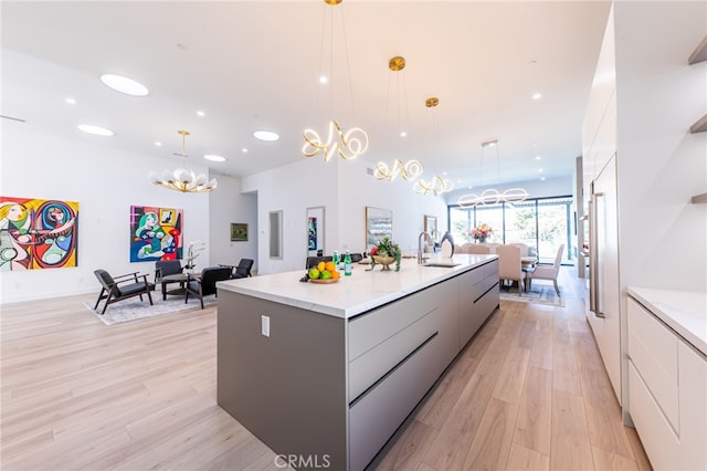 kitchen featuring an island with sink, light wood-type flooring, pendant lighting, white cabinets, and sink