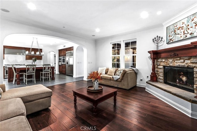 living room with dark wood-type flooring, crown molding, and a stone fireplace