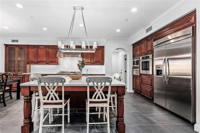 kitchen with decorative light fixtures, appliances with stainless steel finishes, an island with sink, and ornamental molding