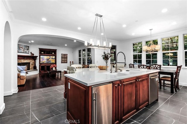 kitchen with decorative light fixtures, a kitchen island with sink, a fireplace, ornamental molding, and sink