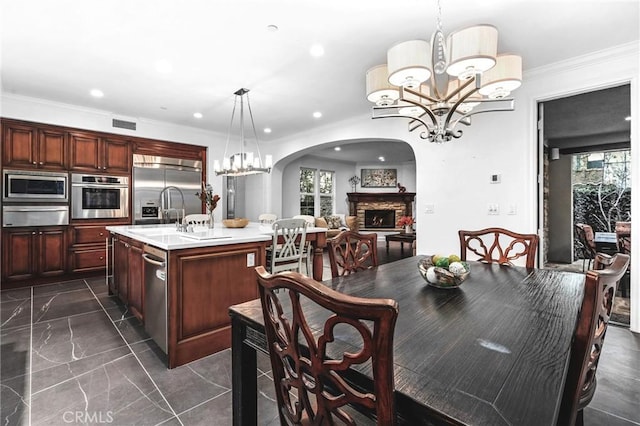 dining area with crown molding, a fireplace, sink, and an inviting chandelier