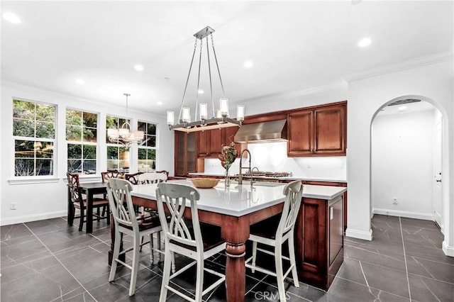 kitchen featuring an island with sink, a breakfast bar area, wall chimney exhaust hood, pendant lighting, and crown molding