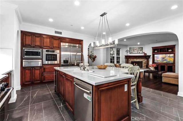 kitchen featuring a fireplace, sink, built in appliances, hanging light fixtures, and a kitchen island with sink