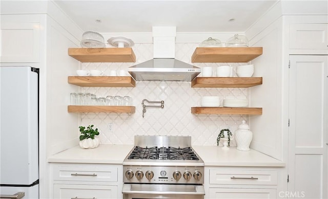 kitchen with white cabinets, stainless steel gas stove, wall chimney range hood, and white refrigerator