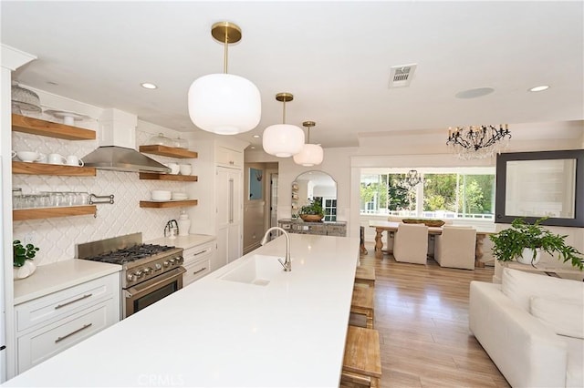 kitchen featuring extractor fan, high end stove, sink, white cabinetry, and hanging light fixtures