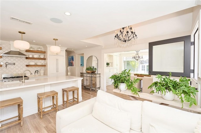 kitchen with decorative light fixtures, backsplash, light hardwood / wood-style floors, a kitchen bar, and a chandelier