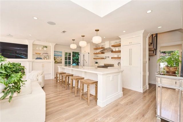 kitchen featuring white cabinetry, a kitchen bar, an island with sink, pendant lighting, and light hardwood / wood-style flooring