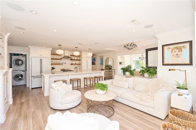 living room with light hardwood / wood-style floors, sink, stacked washer / drying machine, and a chandelier