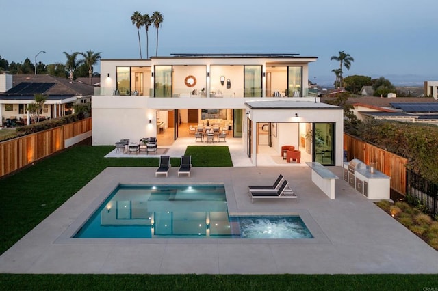 back house at dusk featuring exterior kitchen, a patio area, a pool with hot tub, and an outdoor bar