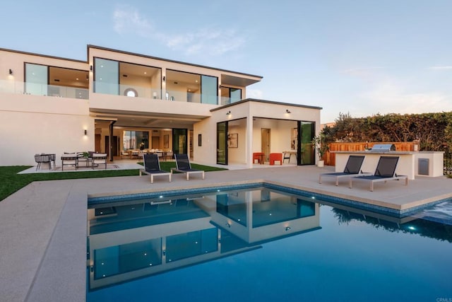 rear view of property with a fenced in pool, a balcony, exterior kitchen, and a patio